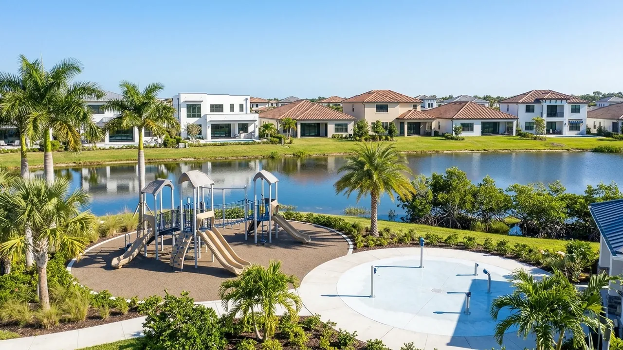 An empty community playground and splash pad beside a lake with new homes behind in a master-planned Southwest Florida neighborhood, sunny day